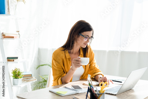 beautiful freelancer working on laptop with coffee cup in home office photo
