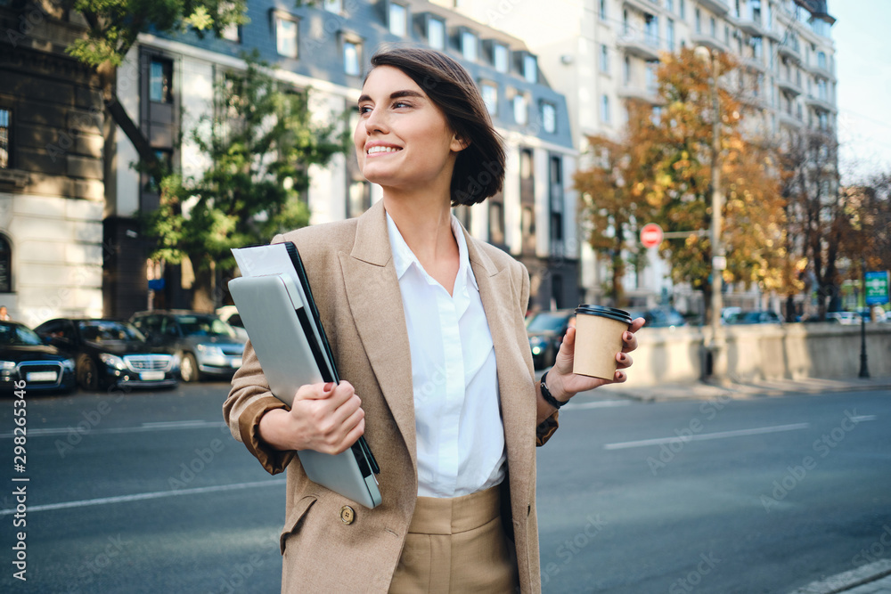 Young beautiful happy businesswoman with laptop and coffee to go on street