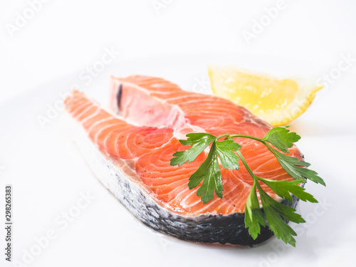 Raw salmon fillet on white studio background decorated with a lemon wedge and some parsley. Side view