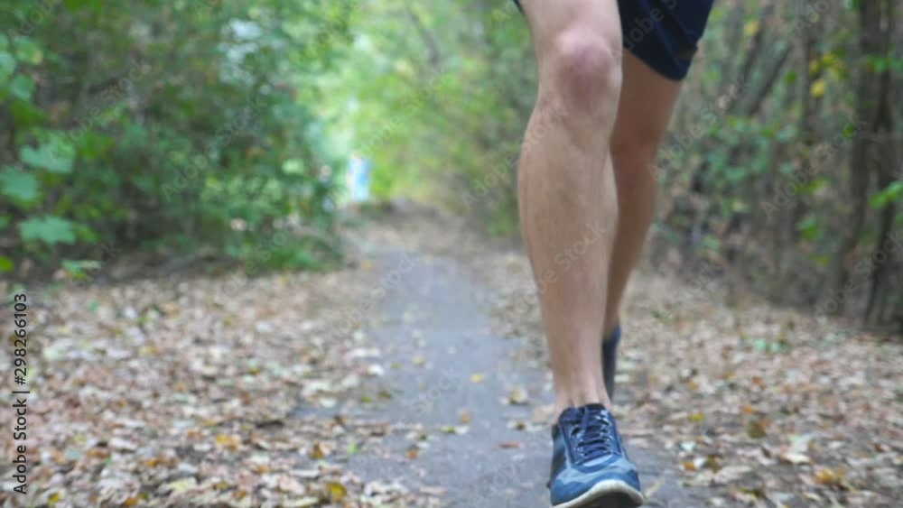 Close up legs of sporty man running along trail in early autumn forest. Male feet of young athlete jogging along path at nature. Strong sportsman exercising outdoor. Healthy active lifestyle. Slow mo Close up legs of sporty man running along trail in early autumn forest. Male feet of young athlete jogging along path at nature. Strong sportsman exercising outdoor. Healthy active lifestyle. Slow mo