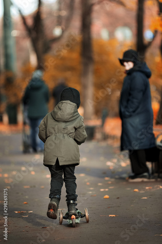 child riding a scooter. The boy rides in the autumn park on a scooter in a hat and jacket