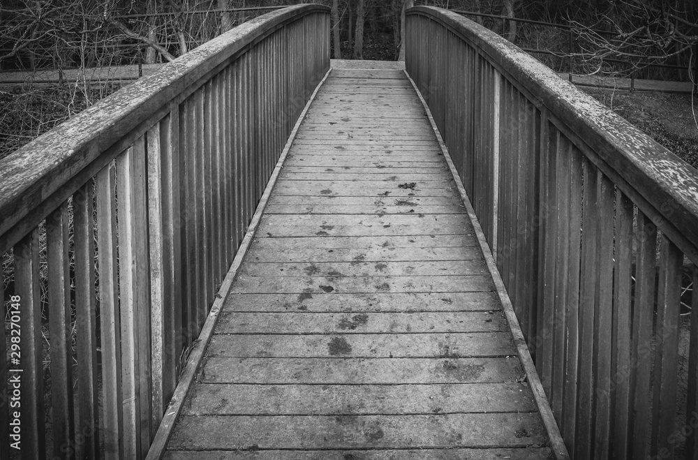 Abstract view of a timber-built footbridge showing detail of the design and construction. Spanning an inland river, the bridge is located in a forest clearing within the UK. Abstract view of a timber-built footbridge showing detail of the design and construction. Spanning an inland river, the bridge is located in a forest clearing within the UK.
