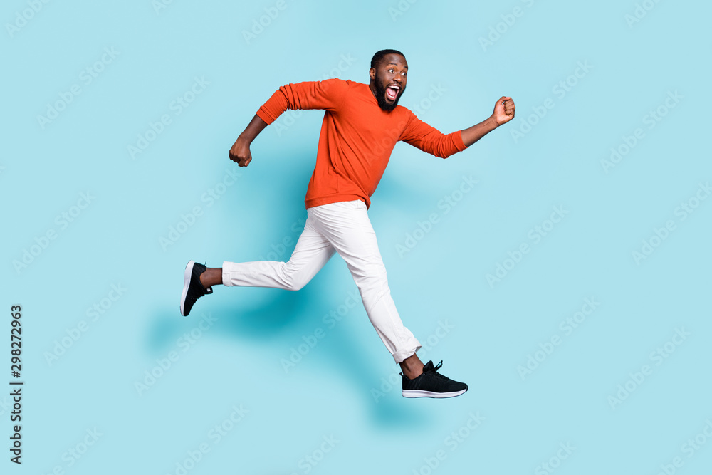 Photo of cheerful positive excited crazy running jumping black man wearing sneakers white trousers pants aspiring for sales isolated vivid blue color background