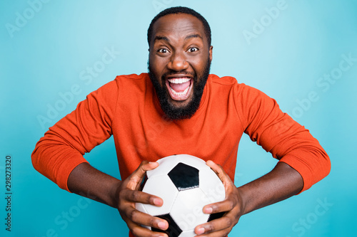 Portrait of cheerful excited mixed-race overjoyed ecstatic man holding ball rejoicing in goal of his favorite team isolated over blue vivid color background