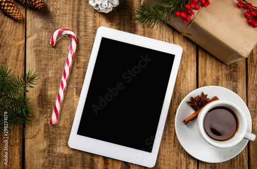 Mock up blank empty screen of tablet on the wooden background with colorful holiday's decoration, tea and gifts. Copyspace, negative space for your advertising. 31 of December, New Year concept.