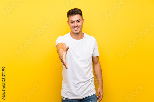 Young handsome man over isolated yellow background shaking hands for closing a good deal