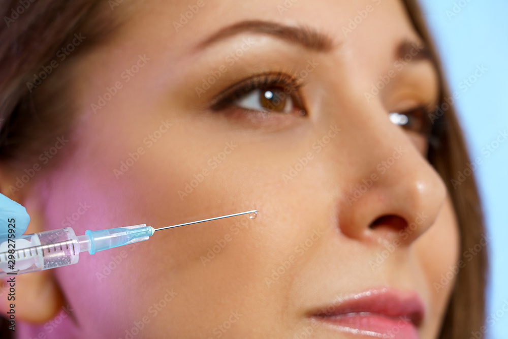 Syringe for beauty injection on the background of the face of a girl close-up. Beautiful female model with healthy skin Syringe for beauty injection on the background of the face of a girl close-up. Beautiful female model with healthy skin