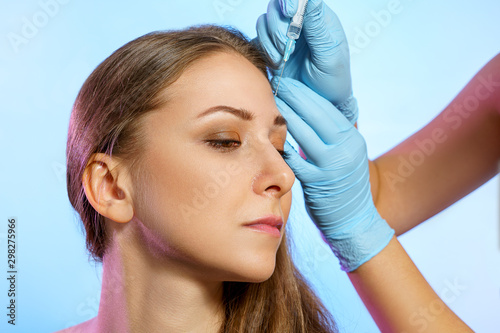 Portrait of beautiful young girl in beauty parlor. Cosmetology injections, hands in medicine gloves holds syringe