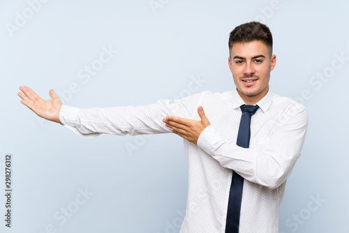 Handsome businessman over isolated blue background extending hands to the side for inviting to come