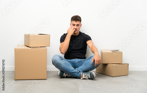 Handsome young man moving in new home among boxes nervous and scared