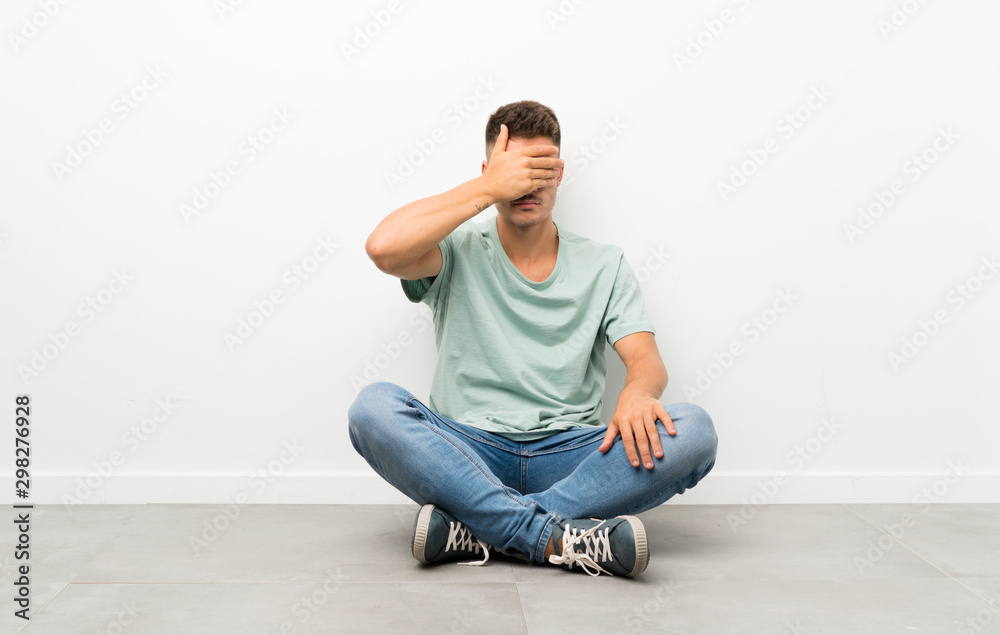 Young handsome man sitting on the floor covering eyes by hands Young handsome man sitting on the floor covering eyes by hands