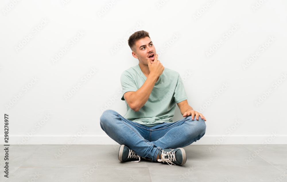 Young handsome man sitting on the floor thinking an idea Young handsome man sitting on the floor thinking an idea