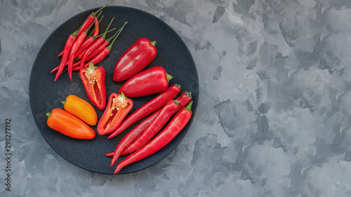 Colorful mix of the freshest and hottest chili peppers and Bulgarian colored pepper on a black plate.