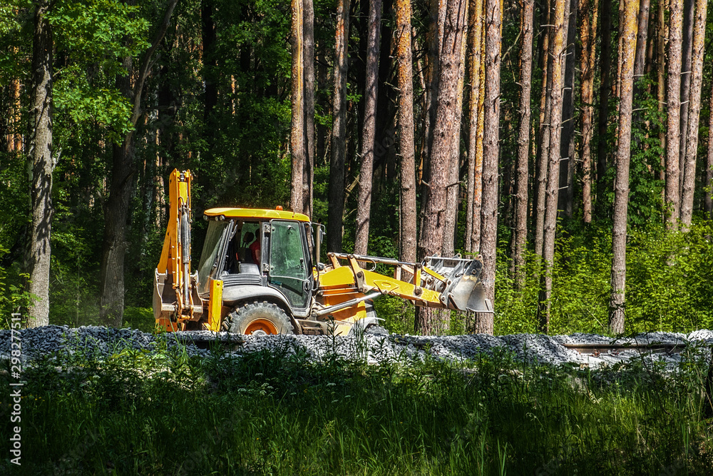 Excavator works on the construction of the railway in the forest. Yellow excavator pours the gravel between the sleepers Excavator works on the construction of the railway in the forest. Yellow excavator pours the gravel between the sleepers