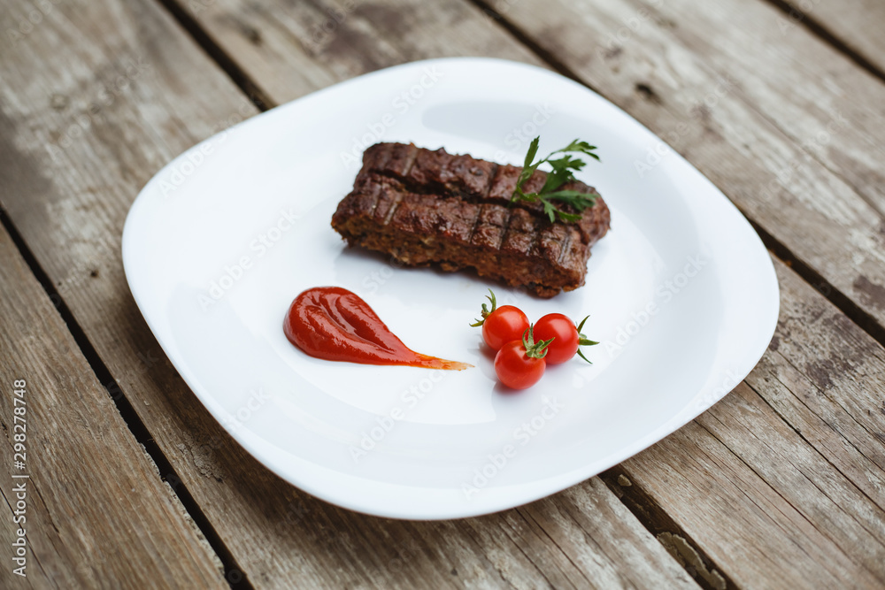 Food in the restaurant. Grilled pork with cherry tomatoes. White plate on a wooden bottom. Food in the restaurant. Grilled pork with cherry tomatoes. White plate on a wooden bottom.