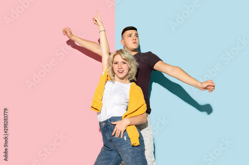 Young emotional man and woman in bright casual clothes posing on pink and blue background. Concept of human emotions  facial expession  relations  ad. Beautiful caucasian couple dancing together.