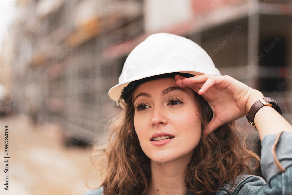 Portrait of a tired young female factory worker wearing a white protective helmet Portrait of a tired young female factory worker wearing a white protective helmet