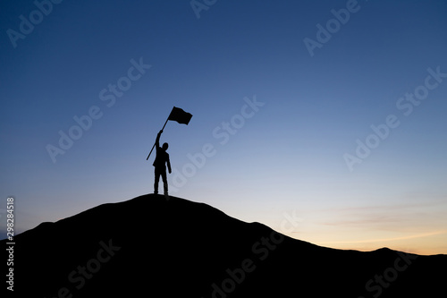 Silhouette of businessman holding a flag on top mountain, sky and sun light background. Business success and goal concept. © cofficevit