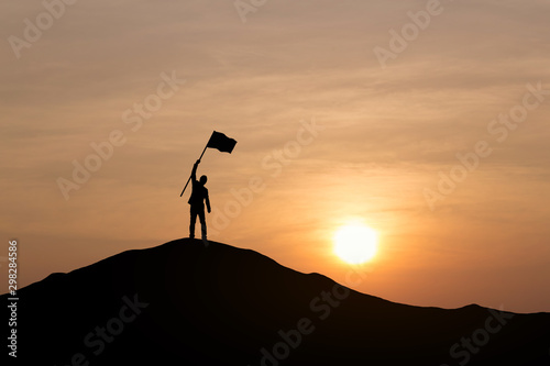 Silhouette of businessman holding a flag on top mountain, sky and sun light background. Business success and goal concept.
