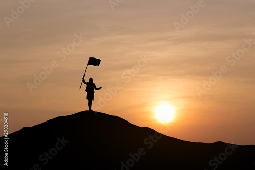 Silhouette of businesswoman holding a flag on top mountain, sky and sun light background. Business success and goal concept.