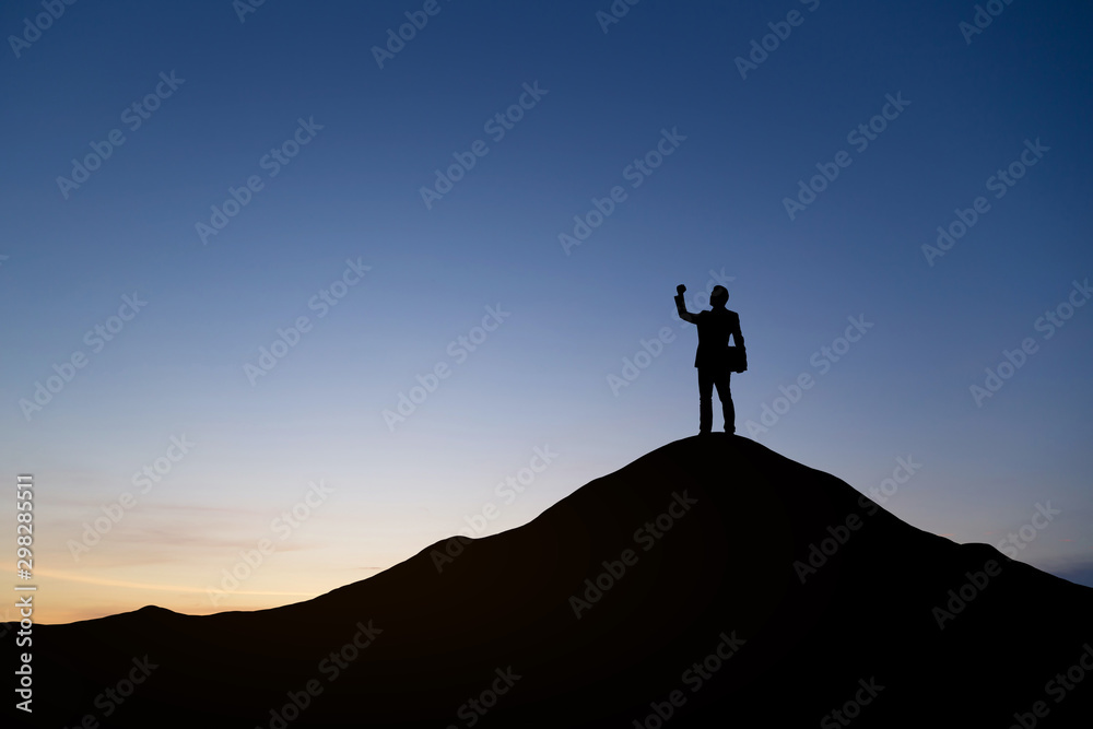 Silhouette of businessman raising his hand to celebrate success on top mountain, sky and sun light background. - obrazy, fototapety, plakaty 