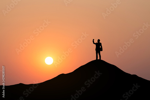 Silhouette of businessman raising his hand to celebrate success on top mountain, sky and sun light background.