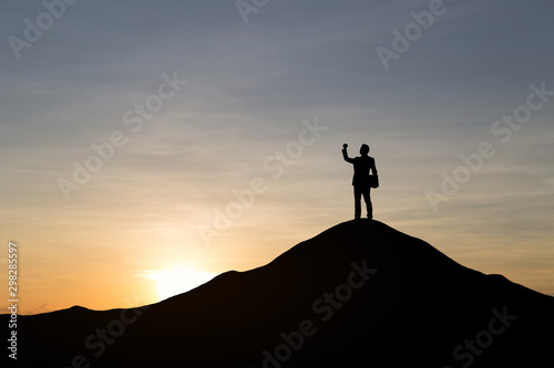 Silhouette of businessman raising his hand to celebrate success on top mountain, sky and sun light background. © cofficevit