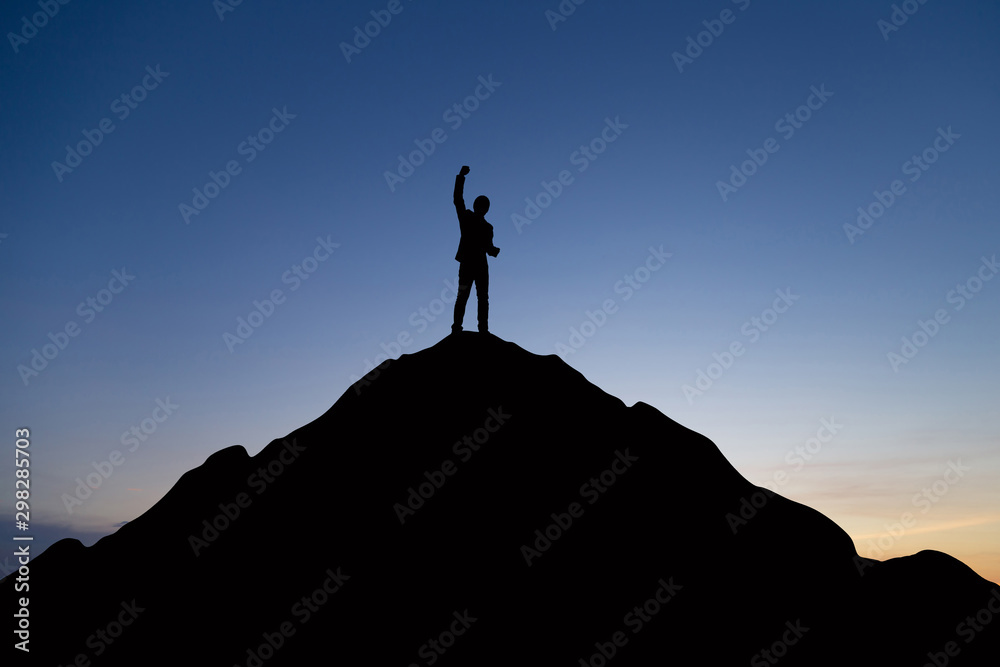 Silhouette of businessman raising his hand to celebrate success on top mountain, sky and sun light background.