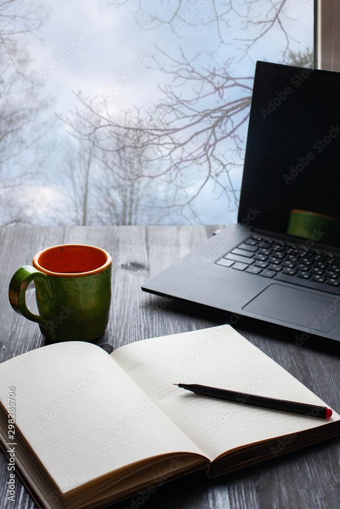 Mug of black coffee on a dark wooden background, opened laptop and notebook nearby. Top view Mug of black coffee on a dark wooden background, opened laptop and notebook nearby. Top view