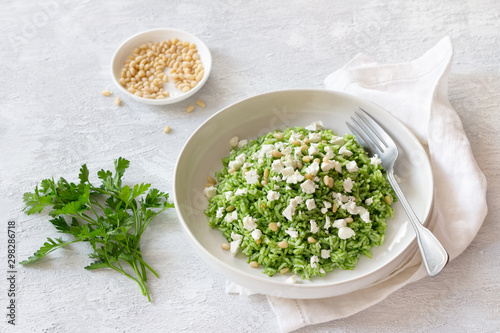 Vegan rice with green oil, pine nuts, cheese in a white bowl on gray background, free space. delicious healthy homemade food 