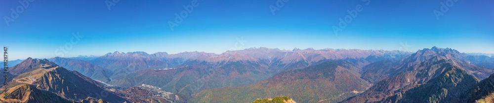 Wide panoramic day view of the mountain valley and mountain peaks in the distance with a clear sky.