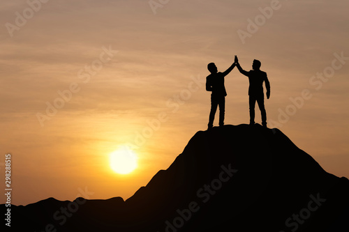 Silhouette of people are celebrating success at the top of the mountain, sky and sun light background. Team business concept.