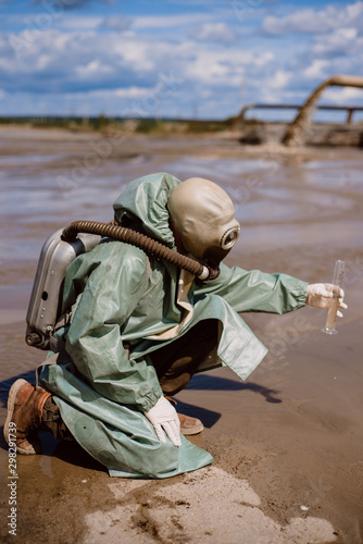 A scientist takes a sample of water from a reservoir after the release of chemical waste. A man in a respirator and a green protective suit from radiation. Water analysis experts. Mask.