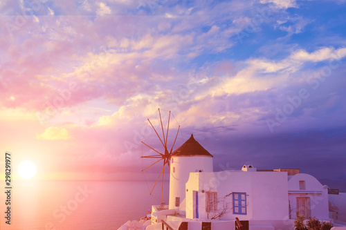 Traditional white windmill in Oia village on Santorini, Greece, on sunset with Sun setting through dramatic heavy clouds