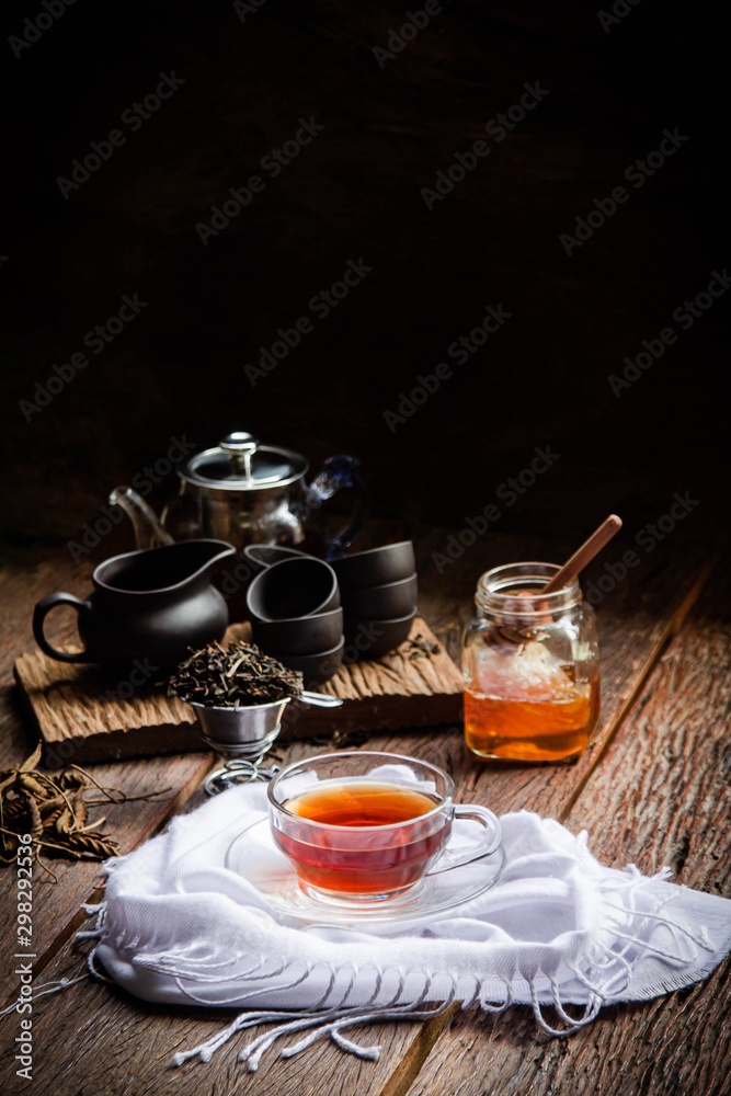 Hot tea in a glass teapot and tea cup with a jar of honey on a black background Hot tea in a glass teapot and tea cup with a jar of honey on a black background