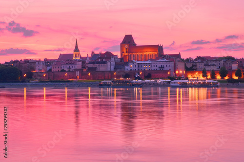 Torun old town in Poland, UNESCO world heritage site, with illumination, reflected in Vistula river on pink sunset. photo