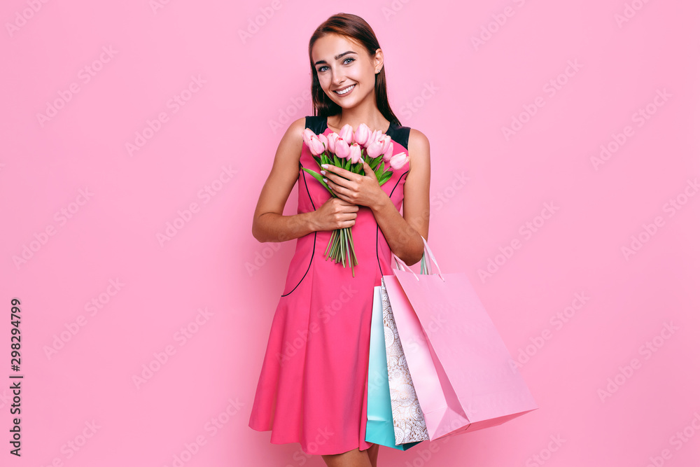 Attractive young girl in a dress with a bouquet of flowers, and shopping on a pink background. Attractive young girl in a dress with a bouquet of flowers, and shopping on a pink background.