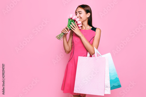 Attractive young girl in a dress with a bouquet of flowers, and shopping on a pink background.