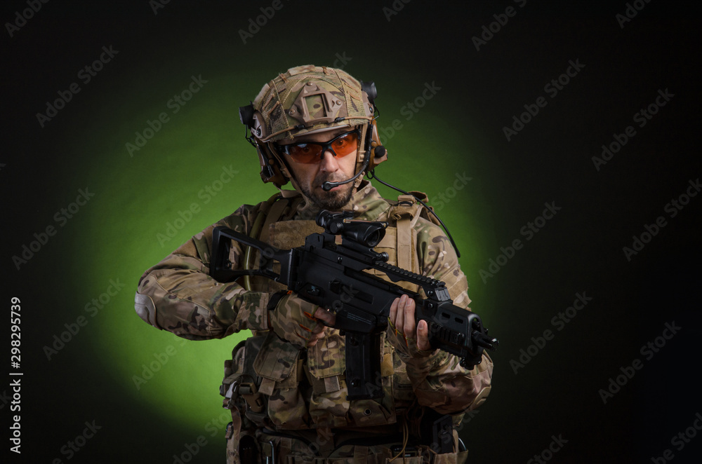 Fototapeta premium a male soldier in military clothes with a weapon on a dark background