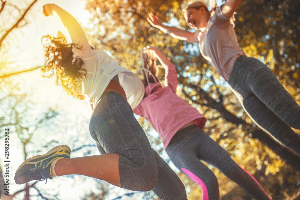 Group of female friends jump around at the city park.Relaxing and making fun after jogging. - obrazy, fototapety, plakaty 