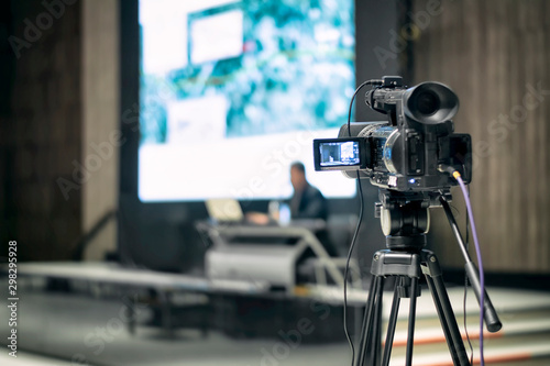 The back view of a professional digital video camera is recording video a presentation event.