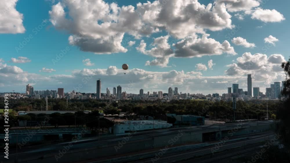 Timelapse clip of a hot air baloon, taking rides into the cloudy blue sky. fast motion of cars and trains in foreground. Tel Aviv downtown skyline in the background. Timelapse clip of a hot air baloon, taking rides into the cloudy blue sky. fast motion of cars and trains in foreground. Tel Aviv downtown skyline in the background.