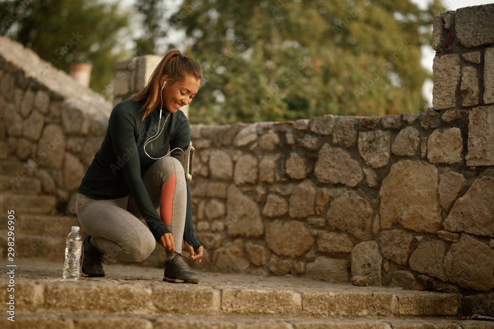 Happy athletic woman tying shoelace before the workout in nature.