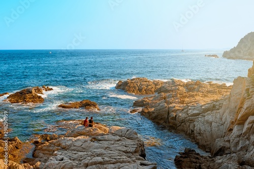 Landscape with sea and couple on a rocky coast at sunset