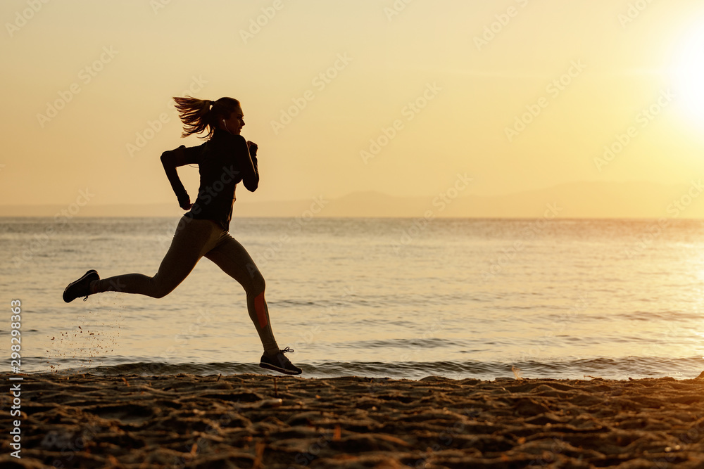 Dedicated female runner jogging at the beach at sunrise.