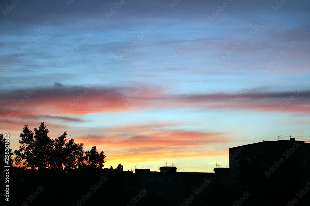Blue-violet-orange sunset over black silhouettes of houses