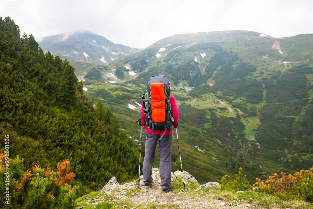 Hiker with backpack and trekking sticks on top of mountain admiring the view