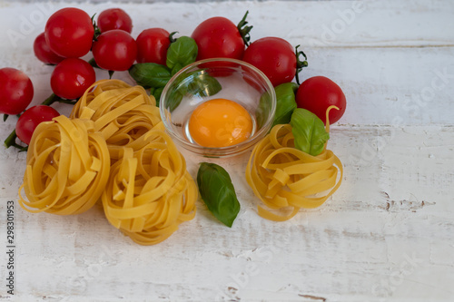 Ingredients for cooking Italian pasta. Pasta, basil, cheese, cherry tomatoes, olive oil, egg, yolk. On a dark background. Copy space.