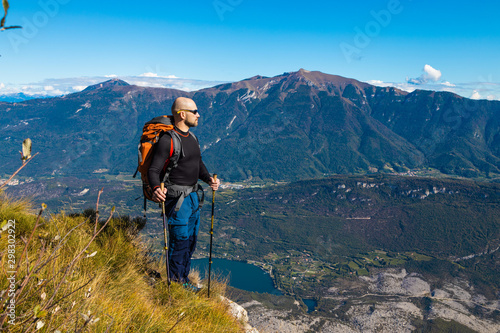 A man traveler with a backpack stands on a hill of beautiful alpine landscape