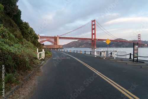 Side View Of The Golden Gate Bridge With Leading Road And Mountains In The Early Morning Hours.